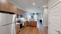 This thoughtfully designed 1-bedroom, 1-bathroom residence makes efficient use of its single-floor layout, offering a cohesive and comfortable living experience throughout. The open-concept kitchen and living area forms the heart of the home, featuring warm wood-tone cabinetry, granite countertops, a classic subway tile backsplash, and a full suite of stainless steel appliances including a range, microwave, dishwasher, and refrigerator. Light wood-style flooring extends across the main living areas, lending a clean and modern aesthetic. The living room is bright and inviting, benefiting from large windows dressed with elegant curtains that filter natural light. A glass-panel door provides additional access and light to the space. The entry hallway offers a clean transition into the home with recessed lighting and easy access to the closet. The bedroom is a calm retreat, featuring plush carpet, generous windows with blinds and drapes, and a dedicated walk-in closet outfitted with wire shelving for organized storage. The bathroom is finished with wood-look flooring, a granite-topped vanity with wood cabinetry, and a tub-shower combination surrounded by white subway tile. Every detail reflects a modern, functional design sensibility.