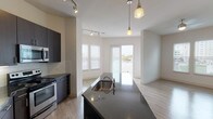 The Cosmopolitan presents a well-appointed 2-bedroom, 2-bathroom residence designed with a modern aesthetic and functional layout. The open-concept kitchen serves as the heart of the home, showcasing dark espresso cabinetry, granite countertops, a subway tile backsplash, stainless steel appliances including a side-by-side refrigerator with ice maker, range, and microwave, along with a generously sized island with a built-in sink and pendant lighting overhead. Track lighting adds a contemporary touch to the kitchen and living area. The living space flows seamlessly from the kitchen, featuring light hardwood-style flooring and a ceiling fan, with sliding glass doors opening to a private balcony that offers views of the surrounding cityscape. Both bedrooms are carpeted and bathed in natural light, with ceiling fans and access to outdoor views. One bedroom features a sliding glass door to a balcony with city views. Each bathroom is finished with dark wood vanities, granite countertops, and hardwood-style flooring. The second bathroom offers a well-lit vanity with a large mirror. Throughout the residence, neutral tones and clean lines create a bright, cohesive atmosphere suited to modern urban living.