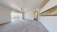 This single-floor residence offers a thoughtfully laid-out interior with a clean, neutral palette and an abundance of natural light. The spacious living area is anchored by plush wall-to-wall carpeting and a ceiling fan with light fixture, while a full-width sliding glass door with vertical blinds opens to an outdoor space, creating a seamless indoor-outdoor connection. A practical pass-through or built-in counter feature adds functionality near the living space.

The galley-style kitchen is efficiently designed with white cabinetry, dark countertops, wood-look vinyl flooring, and a full suite of black appliances including a refrigerator, range, microwave, and dishwasher. Adjacent to the kitchen, a dedicated laundry room provides added convenience with washer and dryer included and continued wood-look flooring.

The bedrooms are generously sized, each featuring soft carpeting, ceiling fans, and vertical blinds over windows that invite ample daylight. Raised ceilings in several rooms enhance the sense of openness. The bathroom is clean and functional, offering a single-sink vanity with dark countertops, white cabinetry, a tiled tub-shower combo, and wood-look flooring. Throughout, the space maintains a bright, move-in-ready aesthetic with crisp white walls and consistent finishes.