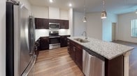 The Ruby is a thoughtfully designed two-bedroom, two-bathroom residence laid out on a single floor. The kitchen serves as a focal point, showcasing rich dark cabinetry paired with granite countertops, a large center island with a built-in sink, pendant lighting overhead, a white tile backsplash, and a full suite of stainless steel appliances. Wood-look flooring flows throughout the main living areas, adding warmth and continuity to the open layout.

Both bathrooms feature the same dark cabinetry and granite vanity countertops found in the kitchen, creating a cohesive aesthetic. Light tile flooring contrasts with the darker fixtures, and one bathroom includes an extended vanity with dual mirrors and overhead lighting, while the other offers direct access to a well-organized walk-in closet with built-in shelving and hanging rods.

The two bedrooms are carpeted for comfort and include ceiling fans and windows that allow natural light to fill each room. One bedroom features a spacious walk-in closet with a multi-tier shelving system. Throughout the residence, neutral tones, recessed lighting, and consistent finishes create a clean, modern ambiance.
