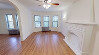 This well-appointed single-floor residence showcases a blend of classic architectural character and functional design. The living area serves as the centerpiece of the home, highlighted by an elegantly detailed white ornamental fireplace, warm hardwood floors, and a graceful arched doorway that connects the space to the rest of the unit. A bay window configuration floods the room with natural light and offers leafy outdoor views, while a ceiling fan and decorative crown molding add to the refined ambiance.

Multiple bedrooms carry the same warm hardwood flooring and are each equipped with ceiling fans, double-hung windows with outdoor greenery views, and cast-iron radiators that speak to the home's historic character. Panel-style wainscoting accents the walls in several rooms, reinforcing the traditional aesthetic throughout.

The kitchen is efficiently laid out with warm wood cabinetry, granite-look countertops, a stainless steel sink, and a full suite of white appliances including a gas range, dishwasher, and refrigerator. A window above the counter brings in natural light.

The bathroom continues the granite countertop theme with a vanity sink, mirrored medicine cabinet, and a tub-shower combination, keeping the space clean and functional. Overall, the residence offers a cohesive, classic character with comfortable, well-lit rooms throughout.