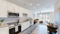 Located at 523 S Madison Ave in Greenwood, Indiana, this thoughtfully designed single-floor residence offers a comfortable and modern living experience. The open-concept layout seamlessly connects the kitchen and living room, creating a bright and functional shared space. The kitchen is well-equipped with crisp white shaker cabinetry extending to the ceiling, stainless steel appliances including a range, microwave, dishwasher, and refrigerator, complemented by neutral quartz-style countertops and a subtle tile backsplash. Light wood-style flooring flows throughout the entire unit, enhancing the cohesive, contemporary aesthetic. The living area is bathed in natural light from a large sliding glass door that opens to an outdoor balcony, with a ceiling fan adding comfort overhead. The bedroom is a calm and spacious retreat, featuring dual windows for natural light, a ceiling fan, and generous proportions for furniture arrangement. The full bathroom includes a tub-shower combination with tile surround, a white vanity, and wood-style flooring that ties into the rest of the unit. Two closets provide ample storage, and a dedicated laundry area adds everyday convenience. Recessed lighting throughout and a neutral color palette give the space a clean, modern character.