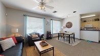 Located at 1822 N Perkins Rd in Stillwater, Oklahoma, this single-floor unit offers a thoughtfully designed layout that balances comfort and functionality. The open-concept living and dining area is a welcoming centerpiece, featuring carpet flooring, a ceiling fan with lighting, track lighting, and multiple large windows dressed with teal curtains that invite abundant natural light. The living space comfortably accommodates both a seating area with a sofa and armchair and a dedicated dining area with a table and chairs, making it ideal for both relaxing and entertaining. A curated gallery wall adds personality to the space. The kitchen is equipped with ample cabinetry featuring dark hardware, granite-style countertops, hardwood-style flooring, and full-size appliances including a refrigerator. A convenient laundry area is accessible nearby. The bedroom is a comfortable retreat with carpet flooring, a window with curtains providing natural light, and space for a dedicated desk area — ideal for studying or working from home. Two bathrooms serve the unit: one features a double-sink vanity with light wood cabinetry and a separate shower, while the second is a compact full bath with overhead storage. Throughout, the neutral gray palette and modern fixtures create a cohesive, contemporary ambiance.