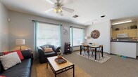 Located at 1822 N Perkins Rd in Stillwater, Oklahoma, this single-floor unit offers a thoughtfully designed layout that balances comfort and functionality. The open-concept living and dining area is a welcoming centerpiece, featuring carpet flooring, a ceiling fan with lighting, track lighting, and multiple large windows dressed with teal curtains that invite abundant natural light. The living space comfortably accommodates both a seating area with a sofa and armchair and a dedicated dining area with a table and chairs, making it ideal for both relaxing and entertaining. A curated gallery wall adds personality to the space. The kitchen is equipped with ample cabinetry featuring dark hardware, granite-style countertops, hardwood-style flooring, and full-size appliances including a refrigerator. A convenient laundry area is accessible nearby. The bedroom is a comfortable retreat with carpet flooring, a window with curtains providing natural light, and space for a dedicated desk area — ideal for studying or working from home. Two bathrooms serve the unit: one features a double-sink vanity with light wood cabinetry and a separate shower, while the second is a compact full bath with overhead storage. Throughout, the neutral gray palette and modern fixtures create a cohesive, contemporary ambiance.