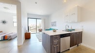 Located at 3425 Motor Ave in the Palms neighborhood of Los Angeles, this modern one-bedroom, one-bathroom unit offers a thoughtfully designed open-concept layout with clean lines and contemporary finishes throughout. Polished concrete flooring runs through the main living areas, adding an industrial-chic aesthetic that complements the crisp white walls and abundant natural light.

The kitchen serves as a functional centerpiece, featuring a wood-toned island with a white quartz countertop, stainless steel appliances including a gas range, microwave, refrigerator, and dishwasher, along with sleek white upper cabinets and warm wood lower cabinetry. The island provides seating and flows naturally into the living area, creating an ideal space for both cooking and entertaining.

The living room is bright and airy, anchored by large floor-to-ceiling sliding glass doors that open onto a private balcony with open views of the surrounding Los Angeles neighborhood — a standout feature that brings the outdoors in.

The bedroom is a comfortable retreat with a large black-framed window that draws in natural light, and a frosted-glass sliding closet that adds a modern touch. The bathroom includes a dark wood vanity, a combination tub and shower, and a stacked in-unit washer and dryer conveniently located nearby. This well-appointed unit balances modern design with practical urban living.