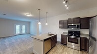 This single-floor residence is designed with an open and functional layout that integrates the kitchen and living areas seamlessly. The kitchen serves as a central hub, showcasing dark espresso cabinetry with ample storage, granite countertops, and a full suite of stainless steel appliances including a refrigerator, electric range, microwave, and dishwasher. A peninsula island with pendant lighting overhead provides additional workspace and a natural division between the kitchen and the living area. Wood-look flooring runs throughout the kitchen, transitioning to plush carpeting in the living spaces.

The living area is generously proportioned, finished with crown molding and neutral wall tones that create a bright, welcoming atmosphere. A set of French doors opens to a private balcony, bringing in natural light and outdoor views. The bedroom features ceiling fans, a walk-in closet, and access to an additional room, offering flexible use of space. A secondary carpeted bedroom includes a ceiling fan and a window with natural light. The bathroom is clean and straightforward, equipped with a walk-in shower, toilet, and wood-look flooring, maintaining a consistent, modern aesthetic throughout the unit.