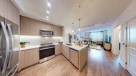 This thoughtfully designed single-floor residence combines modern aesthetics with functional living. The open-concept kitchen is a standout feature, outfitted with light wood cabinetry extending to the ceiling, a subway tile backsplash, white quartz countertops, and a full suite of stainless steel appliances including a range, built-in microwave, and dishwasher. A peninsula with a undermount sink provides additional prep space and naturally connects the kitchen to the rest of the living area. Track lighting and elegant pendant fixtures illuminate the space throughout. The dining area offers an intimate setting with clean white walls, ideal for displaying artwork. The living room is bright and welcoming, benefiting from large windows that invite natural light and feature a hardwood floor that runs continuously through the main living spaces. The bedroom is a serene retreat, offering access to both a private bathroom and a dedicated walk-in closet with built-in shelving. The bathroom features large-format marble-look tile on both the floors and tub surround, creating a clean, spa-like atmosphere. Overall, the residence presents a cohesive modern design with warm wood tones, neutral walls, and refined finishes throughout.