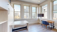 Located at 2–34 Peck St in the heart of Providence, Rhode Island, this single-floor unit offers a thoughtfully designed living space with a clean, contemporary aesthetic set within a historic downtown building. Light wood-tone flooring flows consistently throughout, creating a cohesive and airy feel across all rooms.

The sleeping areas are a standout feature, each equipped with large multi-pane windows that frame sweeping views of Providence's downtown skyline. One bedroom features a built-in Murphy bed with integrated shelving and a bold geometric blue accent wall, maximizing space efficiency without sacrificing style. Another bedroom offers corner window placement, flooding the room with natural light and delivering panoramic city vistas.

The kitchen is outfitted with high-gloss white cabinetry extending to the ceiling, providing ample storage. Stainless steel appliances, including a refrigerator, dishwasher, and microwave, complement the sleek quartz countertops and undermount sink, delivering a fully functional, modern cooking space.

The bathroom features warm wood-toned cabinetry, a wall-mounted vanity mirror with integrated lighting, and large-format slate tile flooring, lending a refined, spa-like quality. The overall design balances urban energy with interior calm, making this a well-appointed space in a prime Providence location.