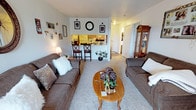 This single-floor unit features a well-organized layout that maximizes its comfortable footprint. The living room serves as the heart of the space, offering room for a full seating arrangement centered around a coffee table, with plush carpeting underfoot that adds warmth to the area. Neutral gray walls keep the space feeling open and versatile.

A defining architectural feature is the pass-through counter connecting the living area to the kitchen, which enhances the open feel while maintaining a distinct cooking zone. The kitchen is equipped with wood-toned cabinetry, a white refrigerator, and tiled backsplash, with bar-height seating along the counter providing a casual dining option.

A hallway visible from the living room leads to the bedroom and bathroom, offering a practical and private separation of sleeping quarters from the main living space. The consistent carpeting throughout the living areas contributes to a cohesive, cozy ambiance. Overall, the unit presents a functional and comfortable single-level layout well-suited for everyday living.