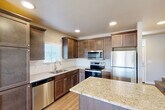 Located in Twin Falls, Idaho, this two-story home offers three bedrooms and three bathrooms across two well-proportioned floors. The main level features an open-concept dining room and kitchen, highlighted by rich dark wood cabinetry, granite countertop surfaces, a stainless steel appliance suite including a refrigerator, range, microwave, and dishwasher, and a center island with additional counter space. Light wood flooring runs throughout the main level, complementing the neutral warm-toned walls and recessed lighting. A sliding glass door in the living area opens to a private patio, bringing in abundant natural light and providing outdoor access. A convenient half bathroom is also located on the main floor. Upstairs, the three bedrooms are carpeted and filled with natural light from windows with blinds. The primary bedroom offers a comfortable, well-proportioned layout. The upper level also includes two full bathrooms, one featuring a tub-shower combination and granite vanity countertop, and a hallway connecting all rooms. A stacked washer and dryer unit is conveniently situated on the upper floor. Multiple closets throughout the home provide ample storage. The staircase features a classic white railing, tying together the clean, neutral aesthetic found throughout the entire home.