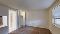 This single-floor residential space presents a straightforward and functional layout designed for comfortable everyday living. The interior is characterized by wall-to-wall carpeting in a warm, neutral tone that adds softness underfoot and contributes to a cozy atmosphere throughout the space. The walls are finished in a clean, light neutral shade, creating a bright and open feel that allows for flexible decorating possibilities. A textured ceiling adds a subtle traditional detail to the overall aesthetic. A notable feature of the space is the closet area equipped with bifold doors, providing practical built-in storage. The open doorway visible in the space suggests a connected layout that allows for easy flow between rooms. Electrical fixtures, including a thermostat and standard outlets, are thoughtfully placed along the walls, reflecting the functional design of the space. The room offers a generous sense of open floor space, making it well-suited for a variety of furniture arrangements. Overall, the space presents a clean, move-in-ready environment with a simple, classic interior style that provides a versatile foundation for personalization.
