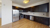 Located at 221 Bergen Street in Harrison, NJ, this single-floor residence offers a thoughtfully designed layout with modern finishes throughout. The kitchen is a standout feature, boasting rich dark espresso cabinetry that extends to the ceiling for ample storage, contrasted by crisp white countertops and a classic white subway tile backsplash. A full suite of stainless steel appliances — including a French door refrigerator, gas range, built-in microwave, and dishwasher — provides a polished, functional cooking space. Light hardwood-style flooring runs throughout the kitchen and living areas, lending a warm, cohesive feel. The walk-in closet is generously proportioned, featuring wire shelving along multiple walls and plush carpeting underfoot, offering excellent storage and organization potential. The bathroom is clean and bright, finished with large white subway tiles in a soaking tub/shower combination with chrome fixtures and a built-in corner shelf. The overall aesthetic of the space balances contemporary design with practical functionality, creating a comfortable and well-organized living environment.
