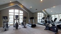 Located at 5885 Tuttle's Grove Blvd in Dublin, Ohio, this fitness center offers a well-appointed space designed to support an active lifestyle. The single-floor layout is defined by striking vaulted ceilings that rise to a dramatic peak, giving the room a spacious, open feel. Large arched windows line the walls, flooding the interior with natural light and providing views of the surrounding greenery, creating an inviting atmosphere for exercise. The neutral-toned walls and patterned carpet complement the clean, modern aesthetic throughout. A full wall of mirrors on one side visually expands the space while allowing users to monitor their form during workouts. The facility is equipped with a variety of cardio machines, including treadmills, ellipticals, and stationary bikes, strategically arranged to maximize floor space and comfort. Recessed lighting supplements the natural light, ensuring the room remains bright at any time of day. The overall ambiance is calm and functional, striking a balance between practicality and comfort. This fitness center provides residents a convenient and well-maintained venue to maintain their health and wellness routines without leaving the community.