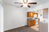 This single-floor residence offers a practical and comfortable layout across several well-defined living areas. The open living area is finished with plush wall-to-wall carpeting and features a ceiling fan with integrated lighting, creating a relaxed and functional atmosphere. A pass-through opening connects the living space directly to the kitchen, enhancing the open feel between the two areas.

The kitchen is efficiently designed with warm wood-toned cabinetry lining both sides of the galley-style space. Dark laminate countertops provide generous prep areas, while white appliances — including a gas range, over-the-range microwave, and full-size refrigerator — are neatly integrated. Light tile flooring and recessed ceiling lights complete the kitchen's clean, functional look.

The bedrooms are spacious and carpeted, each benefiting from large windows dressed with vertical blinds that allow natural light to filter in. Built-in closets with sliding mirrored doors offer ample storage. One bedroom features a distinctively tray-accented ceiling detail, adding subtle architectural interest.

The bathroom is finished with white tile flooring, a single-sink vanity with wood cabinetry, a large mirror with overhead lighting, and a full tub-and-shower combination with tile surround — all presented in a clean, neutral palette.
