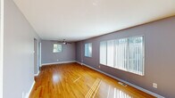 This single-floor, 1-bedroom, 1-bathroom residence offers a practical and comfortable layout designed to maximize its well-proportioned footprint. The spacious living room is a standout feature, showcasing warm hardwood flooring, soft grey walls with crisp white trim, and generous windows dressed with vertical blinds that invite abundant natural light. A ceiling fan overhead and a wall-mounted AC unit provide year-round comfort. The open sightlines from the living area lead seamlessly toward the kitchen, which is equipped with warm oak cabinetry extending to the ceiling, dark granite countertops, tile flooring, and stainless steel appliances including a refrigerator and range. The bedroom continues the consistent hardwood flooring and grey color palette, offering a comfortable retreat with a ceiling fan, a window with outdoor views, and a bifold closet for convenient storage. The bathroom features tile flooring and tile-surround tub/shower combination, a wood vanity with a dark countertop, and a window for natural ventilation. A hallway connects the rooms efficiently, completing this thoughtfully organized single-level home.