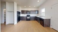 This three-floor home in Bluffdale, Utah offers a well-organized layout across three distinct levels. The ground floor, currently in its unfinished state, features exposed wood-beam ceilings, concrete flooring, and visible insulation — presenting excellent potential for future buildout or additional living space. The main level serves as the heart of the home, highlighted by a well-appointed kitchen with rich dark-stained cabinetry, light quartz-style countertops, black appliances including a refrigerator, range, microwave, and dishwasher, and light hardwood-style flooring that carries throughout the space. The bathroom on this level includes a clean white tiled tub-shower combination. The upper floor houses all three bedrooms, each featuring neutral carpet, white panel doors, and double-door closets for generous storage. The spacious primary bedroom includes a walk-in closet outfitted with built-in shelving and dual hanging rods. Secondary bedrooms benefit from abundant natural light through large windows with blinds, offering views of the surrounding neighborhood. A dedicated utility room and multiple staircases connect the floors efficiently. The home's clean, neutral palette and practical layout make it a versatile and move-in ready residence.