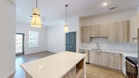 Located at 2800 Milan Court in Birmingham, Alabama, this one-bedroom, one-bathroom unit offers a well-designed layout with contemporary finishes throughout. The kitchen is a standout feature, showcasing light wood-tone cabinetry, a white quartz center island with pendant lighting, a full stainless steel appliance suite including a French door refrigerator, electric range with wall-mounted hood, and dishwasher, all complemented by a white subway tile backsplash and light hardwood-style flooring. The open sightline from the kitchen extends into the living area, creating a connected and functional living space. The bedroom is carpeted and bathed in natural light from a window with blinds, featuring notably tall ceilings that enhance the sense of space. Two gray-toned panel doors lead to the walk-in closet and bathroom, adding a cohesive design touch. The walk-in closet offers built-in shelving, hanging rods, and carpeted flooring, providing generous storage. The bathroom includes light wood vanity cabinetry, a white countertop, a glass-enclosed shower, and wood-look vinyl flooring. A dedicated laundry area accommodates a full-size top-loading washer with an overhead wire shelf, adding everyday convenience to this thoughtfully appointed home.