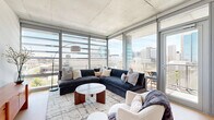 Located in the heart of downtown Phoenix at 440 E Van Buren St, this contemporary 2-bedroom, 3-bathroom residence showcases an industrial-modern aesthetic defined by exposed concrete ceilings, light hardwood flooring, and expansive floor-to-ceiling glass walls. The open-concept living room is a standout space, wrapped in corner glass that frames panoramic views of the Phoenix skyline, flooding the interior with natural light. The kitchen is sleekly appointed with matte gray cabinetry, a subway tile backsplash, stainless steel appliances, and a large quartz waterfall island with bar seating — ideal for both everyday living and entertaining. Both bedrooms feature the signature exposed concrete ceilings and oversized windows with city views, creating a bright yet grounded retreat. The primary bedroom offers a generous layout with direct access to natural light. Three well-designed bathrooms include clean-lined vanities, stone-tiled flooring, and ample storage. A hallway anchors the layout, connecting a dedicated closet and all three bathrooms efficiently. Throughout the residence, architectural details such as the raw concrete surfaces and floor-to-ceiling glazing lend a refined urban loft character, while the elevated position above the city delivers an exceptional sense of openness.