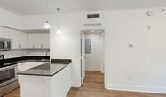 Located at 24801 SW 130th St in Princeton, FL, this well-appointed one-bedroom, one-bathroom unit offers a thoughtfully designed layout across a single floor. The interior is finished with warm wood-look flooring and crisp white walls throughout, creating a clean, modern aesthetic.

The kitchen is a standout feature, showcasing white shaker-style cabinetry, dark granite countertops, a subway tile backsplash, and a full suite of stainless steel appliances including a refrigerator, electric range, and over-the-range microwave. A peninsula with pendant lighting adds both prep space and a casual dining option.

The living room is bright and airy, benefiting from natural light that streams in through sliding glass doors leading to a private balcony — offering pleasant outdoor views of the surrounding greenery. The bedroom is a comfortable size with a dedicated closet for storage. The bathroom features a full tub-shower combination with large-format tile surround, a granite-topped vanity, and coordinating fixtures.

Additional spaces include a hallway, a utility room for added convenience, and a balcony perfect for relaxing outdoors. The unit's efficient floor plan makes excellent use of every square foot, delivering a functional and inviting living environment.