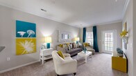 Located at 5300 Patron Pl in North Charleston, SC, this well-appointed 2-bedroom, 3-bathroom single-floor residence offers a thoughtfully designed layout with comfortable living spaces throughout. The open-concept living room features plush carpeting, crown molding, and large windows with access to an outdoor area, allowing natural light to fill the space. The kitchen is equipped with rich dark wood cabinetry, granite-style countertops, black appliances including a refrigerator and range, and tile flooring — all accessible via a columned pass-through that connects seamlessly to the living area. A central hallway links the main living spaces to the private quarters. Both bedrooms are carpeted and generously sized, with the primary bedroom offering ample room for large furnishings and access to a dedicated closet. Each bedroom is served by its own well-appointed bathroom featuring tile flooring, wood vanities with granite-style countertops, and tub-shower combinations. A dedicated in-unit laundry room accommodates a full-size washer and dryer. Two closets provide additional storage. The neutral warm-gray palette and crown molding details throughout lend the space a clean, cohesive aesthetic.