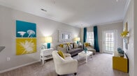 Located at 5300 Patron Pl in North Charleston, SC, this well-appointed 2-bedroom, 3-bathroom single-floor residence offers a thoughtfully designed layout with comfortable living spaces throughout. The open-concept living room features plush carpeting, crown molding, and large windows with access to an outdoor area, allowing natural light to fill the space. The kitchen is equipped with rich dark wood cabinetry, granite-style countertops, black appliances including a refrigerator and range, and tile flooring — all accessible via a columned pass-through that connects seamlessly to the living area. A central hallway links the main living spaces to the private quarters. Both bedrooms are carpeted and generously sized, with the primary bedroom offering ample room for large furnishings and access to a dedicated closet. Each bedroom is served by its own well-appointed bathroom featuring tile flooring, wood vanities with granite-style countertops, and tub-shower combinations. A dedicated in-unit laundry room accommodates a full-size washer and dryer. Two closets provide additional storage. The neutral warm-gray palette and crown molding details throughout lend the space a clean, cohesive aesthetic.