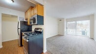 This single-floor unit is thoughtfully laid out across a compact, functional floor plan. The galley-style kitchen is well-equipped, featuring warm honey-toned cabinetry, granite-look countertops, and a full suite of stainless steel appliances including a gas range, over-the-range microwave, dishwasher, and refrigerator. Wood-look flooring runs throughout the kitchen, which opens into a dedicated dining area accented by a modest chandelier and crown molding detail.

The living area is generously sized, featuring neutral wall-to-wall carpeting and a large sliding glass door dressed with vertical blinds that provides access to a balcony and allows ample natural light to fill the space. The textured ceiling and crown molding add architectural character throughout.

The bedroom offers comfortable proportions with soft carpeting, a window with vertical blinds, and a walk-in closet equipped with built-in shelving for organized storage. An additional carpeted room features an exposed duct and window, suitable as a second bedroom or flex space.

The bathroom is cleanly finished with large-format tile surrounding the soaking tub and shower, complemented by a wood-toned vanity and wood-look flooring.