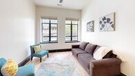 Located in the heart of downtown Winston-Salem, North Carolina, this 2-bedroom, 2-bathroom apartment at 50 West 4th Street offers a well-designed urban living experience. The single-floor layout flows efficiently across a comfortable footprint, with light hardwood flooring and crisp white walls unifying each room throughout.

The open-concept kitchen and living area serves as the central hub of the unit. The kitchen is equipped with stainless steel appliances, rich dark cabinetry reaching toward the soaring ceilings, and a granite-topped island with an undermount sink — ideal for both cooking and entertaining. Track and pendant lighting illuminate the space with a modern touch.

The living room features tall windows with black frames that invite natural light and offer street-level views of the surrounding downtown cityscape. A distinctive arched doorway adds an architectural accent that blends contemporary and classic elements.

Both bedrooms are well-proportioned, with the primary bedroom offering generous space, natural light, wood panel sliding doors, and closet access. The second bedroom mirrors the clean, minimalist aesthetic found throughout the unit.

Each bathroom is outfitted with a standout sculptural glass sink basin in seafoam green, set atop a dark vanity with a boldly framed mirror — providing a distinctive design focal point. The overall ambiance is clean, modern, and urbane.