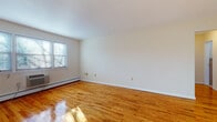 This single-floor residence offers a clean, well-maintained interior defined by warm, polished hardwood floors that extend throughout the living areas and bedrooms, reflecting natural light and lending the space a bright, welcoming character.

The spacious living room is a standout feature, offering generous proportions, crisp white walls, and multiple windows that bathe the room in sunlight. Baseboard heating and a wall-mounted air conditioning unit ensure year-round comfort. A dedicated dining area adjoins the living space, illuminated by a classic chandelier and a window with an outdoor view, making it an ideal spot for meals and gatherings.

The kitchen is equipped with warm honey-toned wood cabinetry, granite-style countertops, a tile backsplash, and white appliances including a gas range and over-the-range microwave. Tile flooring completes the practical and tidy aesthetic of the space.

The bedroom offers a tranquil retreat with the same gleaming hardwood floors and ample wall space. The bathroom is tastefully finished with large-format neutral ceramic tile surrounding a full soaking tub and shower combination, complemented by a white vanity with storage and a mirrored medicine cabinet above.

Throughout the residence, the design emphasizes clean lines, natural light, and functional simplicity.