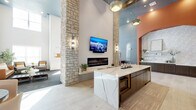 Located at 6773 Campus Dr in Colorado Springs, CO, this beautifully appointed single-floor community lounge offers a generously sized, open-plan living area designed with modern sophistication. The space immediately impresses with its soaring ceilings and dramatic stacked stone columns that anchor the central gathering area, lending a warm, natural texture that contrasts elegantly with the contemporary finishes throughout.

At the heart of the space sits a stunning marble-topped island with deep veining and dark cabinetry beneath, complemented by pendant lighting overhead. A sleek linear fireplace is mounted to the wall between the stone columns, with a flat-screen TV above — creating an inviting focal point for the room. Exposed wood ceiling beams add rustic character to the otherwise modern palette.

The lounge transitions seamlessly into a comfortable seating area featuring plush, mid-century modern furnishings, textured carpet flooring, and large windows that flood the space with abundant natural light. Warm terracotta-toned accent walls and arched architectural details introduce a subtle Southwestern influence, harmonizing beautifully with the neutral gray tones and light tile flooring.

A secondary seating nook near the entry provides an intimate retreat, while the open layout accommodates both casual lounging and social gatherings. The overall ambiance is refined yet welcoming, blending upscale design elements with a relaxed, community-centered atmosphere.