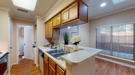 This single-story residence presents a well-organized layout designed for comfortable everyday living. The kitchen is a standout feature, configured in a galley style with warm honey-toned wood cabinetry extending to the ceiling, light speckled countertops, and a double stainless steel sink integrated into a peninsula that opens toward the adjoining living area. Appliances include an electric range with overhead microwave, dishwasher, and full-size refrigerator. A window above the sink allows natural light into the cooking space.

The living areas feature warm hardwood-style flooring and are accented by crown molding and ceiling fans throughout. Vaulted ceilings in the main living space add a sense of openness, while multiple windows fitted with horizontal blinds provide ample natural light. A separate dining or flex area also benefits from dual windows overlooking the exterior.

The bedroom is carpeted and generously sized, featuring crown molding, a ceiling fan, and a mirrored sliding-door closet offering practical storage. The bathroom includes a vanity with light countertops, wood-framed mirror, overhead cabinetry, and a shower-tub combination. Overall, the space presents a cohesive, neutral palette with functional finishes throughout.