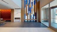 The Six Points Bloomfield Lobby in Bloomfield, NJ, presents a contemporary and well-appointed entrance experience defined by high-end finishes and carefully considered design details. The lobby's most striking feature is a soaring, floor-to-ceiling art installation composed of blue, white, and wood-toned vertical panels, complemented by a sleek linear fireplace set against a marble surround—creating a dramatic focal point upon entry. Terrazzo tile flooring runs throughout, lending a polished, cohesive aesthetic.

A welcoming lounge area features a bold cobalt-blue velvet sofa, marble-topped coffee table, and sculptural pendant lighting suspended from curved ceiling tracks. A decorative geometric partition screen separates the seating area from the reception desk, adding visual depth. Adjacent glass-enclosed meeting rooms provide private conferencing space, outfitted with warm wood surfaces, blue accent walls, and natural light from surrounding windows offering views of the Bloomfield skyline.

The elevator bank features stainless steel cab doors framed by horizontal-striped tile surrounds and illuminated by linear ceiling fixtures. A corridor leads to glass-door building exits, with a glass-walled lounge nook showcasing a distinctive tufted orange accent wall. The overall ambiance is professional yet inviting, balancing bold design elements with functional amenities.