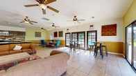 Located at 727 S Lyon St in Santa Ana, California, this single-floor community space offers a welcoming and versatile layout that seamlessly integrates a living room, dining area, and kitchen. The interior is finished with light-toned ceramic tile flooring throughout, contributing to a clean and open atmosphere. Multiple ceiling fans are distributed across the space, ensuring comfortable airflow year-round.

The living area features warm, neutral-toned seating arranged around a woven coffee table, framed artwork, and a wall-mounted television flanked by vibrant turquoise cabinetry, adding a pop of color and character to the room. A sliding glass door opens directly to an outdoor area, inviting in natural light and views of the surrounding grounds.

The dining zone offers a mix of high-top bar tables with industrial-style stools and traditional seating, making it ideal for casual gatherings. A wall of dark-framed French doors floods this area with sunlight and provides direct views of an outdoor pool area, creating a bright and airy ambiance.

The kitchen is well-appointed with dark grey cabinetry, stainless steel appliances, a wood-look tile backsplash, and a granite-topped peninsula. Two-tone walls in warm gold and cream tones tie the entire space together, giving the clubhouse a cohesive, inviting character throughout.