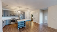 Located at 1941 Roland Clarke Place in Reston, VA, this well-designed 2-bedroom, 2-bathroom residence offers a thoughtful layout across a single floor. The open-concept living room greets you with warm hardwood-style flooring, a striking white brick accent wall, and floor-to-ceiling glass doors that flood the space with natural light and provide access to a private balcony with outdoor views.

The kitchen is a standout feature, showcasing gray shaker-style cabinetry with matte black hardware, quartz countertops, a classic white subway tile backsplash, stainless steel appliances, and a center island with pendant lighting — ideal for both everyday cooking and entertaining.

Both bedrooms are carpeted and bright, each benefiting from large windows with outdoor views. The primary bedroom is generously proportioned and includes a spacious walk-in closet outfitted with custom built-in shelving and dual hanging rods. The second bedroom features its own well-sized closet with wire shelving.

The primary bathroom impresses with a double-sink vanity, illuminated mirrors, wood-look flooring, and a separate glass-enclosed shower. The second bathroom mirrors the modern aesthetic with a tiled tub-shower combo, a quartz vanity, and an LED-backlit mirror. Clean lines and contemporary finishes are consistent throughout the entire residence.
