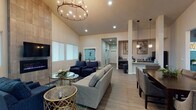 Located at 1090 North Cecil Road in Post Falls, Idaho, this single-story community clubhouse offers a thoughtfully designed gathering space that blends comfort with functionality. The main lounge is the heart of the facility, distinguished by soaring vaulted ceilings, light wood-look flooring, and an eye-catching floor-to-ceiling tiled fireplace surround with a wall-mounted TV. A statement chandelier with exposed Edison-style bulbs anchors the space, casting warm light over a generously sized seating arrangement of neutral sofas and navy accent chairs. An adjacent dining area with a dark wood table and upholstered chairs provides a dedicated space for meals or meetings. A secondary lounge nook features deep navy accent walls, additional seating, and its own chandelier, creating a more intimate atmosphere. Near the entrance, a welcoming reception area with frosted glass office windows and French doors leads into the building. The fitness center is expansive and well-appointed, divided into two connected zones: one housing treadmills, an elliptical, stationary bikes, and exercise balls with mirrored walls, and the other featuring a full dumbbell rack, a flat bench, a wall-mounted TV, and rubber flooring. Large windows throughout the fitness area bring in natural light and views of the surrounding grounds, enhancing the overall sense of openness and energy.