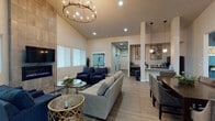 Located at 1090 North Cecil Road in Post Falls, Idaho, this single-story community clubhouse offers a thoughtfully designed gathering space that blends comfort with functionality. The main lounge is the heart of the facility, distinguished by soaring vaulted ceilings, light wood-look flooring, and an eye-catching floor-to-ceiling tiled fireplace surround with a wall-mounted TV. A statement chandelier with exposed Edison-style bulbs anchors the space, casting warm light over a generously sized seating arrangement of neutral sofas and navy accent chairs. An adjacent dining area with a dark wood table and upholstered chairs provides a dedicated space for meals or meetings. A secondary lounge nook features deep navy accent walls, additional seating, and its own chandelier, creating a more intimate atmosphere. Near the entrance, a welcoming reception area with frosted glass office windows and French doors leads into the building. The fitness center is expansive and well-appointed, divided into two connected zones: one housing treadmills, an elliptical, stationary bikes, and exercise balls with mirrored walls, and the other featuring a full dumbbell rack, a flat bench, a wall-mounted TV, and rubber flooring. Large windows throughout the fitness area bring in natural light and views of the surrounding grounds, enhancing the overall sense of openness and energy.