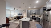 This single-floor residence offers a thoughtfully designed open-concept layout that seamlessly connects the kitchen, dining, and living areas. The kitchen is a standout feature, showcasing grey shaker-style cabinetry extending to the ceiling, granite countertops, a white subway tile backsplash, and a full suite of stainless steel appliances including a refrigerator, range, microwave, and dishwasher. A central island with matching granite and bar seating serves as both a functional workspace and a casual dining spot, illuminated by stylish pendant lights overhead.

The living area is bright and welcoming, with large windows fitted with blinds allowing ample natural light. A ceiling fan enhances comfort, and wood-look flooring flows consistently throughout the space, adding warmth and cohesion. The layout also includes a secondary seating nook with additional window exposure, ideal for a reading corner or flex space.

The bathroom is efficiently designed with a wide granite-topped vanity with grey cabinetry, a shower with a curtain enclosure, and wood-look flooring continuing from the main living areas. A hallway connects the bathroom to the bedroom, maintaining a clean, functional flow throughout the residence. The overall aesthetic is contemporary and neutral, with modern fixtures and finishes creating a polished, cohesive environment.