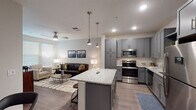 This single-floor residence offers a thoughtfully designed open-concept layout that seamlessly connects the kitchen, dining, and living areas. The kitchen is a standout feature, showcasing grey shaker-style cabinetry extending to the ceiling, granite countertops, a white subway tile backsplash, and a full suite of stainless steel appliances including a refrigerator, range, microwave, and dishwasher. A central island with matching granite and bar seating serves as both a functional workspace and a casual dining spot, illuminated by stylish pendant lights overhead.

The living area is bright and welcoming, with large windows fitted with blinds allowing ample natural light. A ceiling fan enhances comfort, and wood-look flooring flows consistently throughout the space, adding warmth and cohesion. The layout also includes a secondary seating nook with additional window exposure, ideal for a reading corner or flex space.

The bathroom is efficiently designed with a wide granite-topped vanity with grey cabinetry, a shower with a curtain enclosure, and wood-look flooring continuing from the main living areas. A hallway connects the bathroom to the bedroom, maintaining a clean, functional flow throughout the residence. The overall aesthetic is contemporary and neutral, with modern fixtures and finishes creating a polished, cohesive environment.