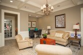 This single-story space in Columbus, Georgia is thoughtfully designed with a refined, traditional aesthetic that balances comfort and functionality. Natural stone tile flooring runs throughout, providing a cohesive and durable foundation across the various areas of the space.

The main living area is a standout feature, showcasing elegant coffered ceilings accented by a decorative chandelier and recessed lighting. Neutral gray walls are complemented by classic wainscoting, creating a polished, timeless atmosphere. A generous seating arrangement anchors the room, which also accommodates a dedicated workspace.

A wall of dark-framed French doors floods the space with natural light and offers clear views of the outdoor surroundings, seamlessly connecting the interior to the exterior environment. The transition area near these doors features a welcoming sitting space with stone tile flooring and a layered area rug.

A compact kitchenette provides practical amenities, including dark wood cabinetry, granite countertops, an undermount sink, and under-cabinet lighting. Adjacent to this is a dining area with wainscoted walls, a multi-pane window, and a counter-height table with seating for four, ideal for casual gatherings or meetings.

Overall, the space exudes a warm, well-appointed character suited for both professional and social use.