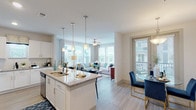 This single-floor residence is thoughtfully designed with an open-concept layout that seamlessly connects the kitchen, dining, and living areas. The kitchen serves as a functional centerpiece, featuring white cabinetry, a subway tile backsplash, stainless steel appliances, and a generous granite-topped island with pendant lighting overhead. Light wood-style flooring flows throughout the main living areas, enhancing the bright, airy atmosphere created by abundant natural light streaming through multiple large windows.

The dining area sits adjacent to the kitchen and offers direct access to a private balcony through glass-paneled doors, making it ideal for indoor-outdoor living. The living room is anchored by a wall of windows that frame outdoor views and is equipped with a ceiling fan for added comfort.

Both bedrooms are carpeted and well-lit with large windows and ceiling fans. The primary bedroom includes balcony access, while both rooms offer ample space for furnishings. The bathroom is elongated and well-appointed, featuring granite countertops, white cabinetry, a dedicated vanity area, and a separate shower. The entryway, finished with light flooring and a double-door closet, provides a clean and welcoming transition into the home.