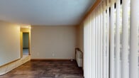 Located at 13804 Ford Ln in Burton, Ohio, this single-floor, two-bedroom, one-bathroom unit offers a practical and efficiently designed layout. The living room features dark hardwood-style flooring, warm neutral walls, a textured ceiling, and a sliding glass door fitted with vertical blinds that opens to an outdoor view of mature greenery, allowing natural light to fill the space. A wall-mounted heating/cooling unit provides climate control in this area.

The open layout connects the living room to the dining area, which is distinguished by light diagonal tile flooring and an overhead pendant chandelier. The adjacent kitchen is well-equipped with light wood cabinetry offering ample storage, a tile backsplash, laminate countertops, a double sink, and black appliances including a refrigerator, dishwasher, and electric range. Light tile flooring continues throughout the kitchen and dining areas.

Both bedrooms are carpeted and finished with neutral walls, wood baseboards, and textured ceilings, providing a quiet and comfortable atmosphere. The full bathroom includes a single-sink vanity, a tiled tub-shower combination, and tile flooring, offering a clean and functional design.