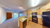 This single-floor residence offers a thoughtfully designed open-concept layout that seamlessly connects the kitchen and living areas. The kitchen is well-equipped with light maple cabinetry, black appliances including a range, built-in microwave, dishwasher, and refrigerator, complemented by a double-basin sink and laminate countertops. Hardwood-style flooring runs throughout the kitchen, transitioning to plush carpeting in the living and bedroom areas. Track lighting overhead provides adjustable illumination throughout the main living space.

The spacious living room is bright and airy, featuring a ceiling fan, neutral-toned walls, and a sliding glass door that opens to a private balcony, offering pleasant outdoor views. The open sightlines between the kitchen and living area create a cohesive and functional common space.

The bedrooms are generously sized, each featuring soft carpeting, ceiling fans, and ample natural light. One bedroom boasts a large window framing a picturesque view of a lush green landscape. The bathroom includes a wood-toned vanity with a white sink, hardwood-style flooring, and clean white walls. Throughout the residence, warm wood-toned interior doors and trim add a cohesive, classic character to the overall design.
