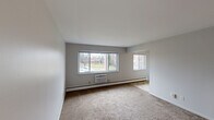 This single-floor, 2-bedroom, 1-bathroom residence offers a practical and comfortable layout designed for everyday living. The living room is the centerpiece of the home, featuring large sliding windows that invite abundant natural light and provide outdoor views of the surrounding grounds. Neutral-toned carpet, clean white walls, and baseboard heating give the space a simple, functional character. A wall-unit air conditioner adds year-round climate control convenience.

The kitchen is outfitted with warm oak cabinetry extending to the upper walls, a white electric range, a full-size refrigerator, and a double-basin sink with ample counter space. Light tile flooring ties the kitchen together and provides easy maintenance underfoot.

Both bedrooms are carpeted and well-proportioned, each featuring baseboard heating and windows with outdoor views. The primary bedroom includes a built-in closet with louvered bifold doors and integrated shelving, offering practical storage. A second hallway closet adds additional storage to the unit.

The bathroom includes a tiled tub-shower combination with accent tiles, a vanity with wooden cabinetry, tile flooring, and a window for natural ventilation. Two hallways connect the rooms efficiently, contributing to a smooth and logical flow throughout the home.