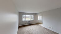 This single-floor, 2-bedroom, 1-bathroom residence offers a practical and comfortable layout designed for everyday living. The living room is the centerpiece of the home, featuring large sliding windows that invite abundant natural light and provide outdoor views of the surrounding grounds. Neutral-toned carpet, clean white walls, and baseboard heating give the space a simple, functional character. A wall-unit air conditioner adds year-round climate control convenience.

The kitchen is outfitted with warm oak cabinetry extending to the upper walls, a white electric range, a full-size refrigerator, and a double-basin sink with ample counter space. Light tile flooring ties the kitchen together and provides easy maintenance underfoot.

Both bedrooms are carpeted and well-proportioned, each featuring baseboard heating and windows with outdoor views. The primary bedroom includes a built-in closet with louvered bifold doors and integrated shelving, offering practical storage. A second hallway closet adds additional storage to the unit.

The bathroom includes a tiled tub-shower combination with accent tiles, a vanity with wooden cabinetry, tile flooring, and a window for natural ventilation. Two hallways connect the rooms efficiently, contributing to a smooth and logical flow throughout the home.