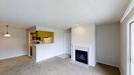 This single-floor residence offers a practical and comfortable layout designed for easy living. The living room serves as the heart of the space, featuring wall-to-wall carpeting that adds warmth underfoot and a classic white-mantled fireplace framed in tile, creating a welcoming focal point. A textured ceiling runs throughout, adding subtle character to the interior.

The kitchen is thoughtfully connected to the living area via a pass-through opening, promoting an open and social atmosphere. Warm wood cabinetry lines the kitchen walls, complemented by essential appliances including a refrigerator, microwave, and range. A tiled countertop bar along the pass-through provides a convenient casual dining or prep surface, while the kitchen floor transitions to tile, offering easy maintenance in the cooking area.

A doorway visible from the main living space leads further into the residence, hinting at additional private areas beyond. The overall color palette is neutral and clean, with white walls and light tones throughout that enhance the sense of brightness and openness. This well-organized single-level layout balances functionality with comfort, making it an inviting and efficient living space.