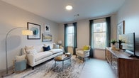 Located at 200 Presidential in Woburn, Massachusetts, this thoughtfully designed single-floor residence offers a seamless blend of modern aesthetics and functional living. The open-concept kitchen is a standout feature, showcasing two-tone cabinetry with crisp white upper cabinets and deep charcoal lower cabinets, quartz countertops, a large center island, tile backsplash, and a full suite of stainless steel appliances. Light wood-style flooring flows throughout the main living areas, enhancing the bright and airy atmosphere. The living room is generously proportioned, featuring large windows dressed with teal accent curtains that invite abundant natural light and offer views of the surrounding neighborhood. Two well-appointed bedrooms provide comfortable retreats; one includes a walk-in closet, while both rooms feature plush carpeting, large windows with sheer drapery, and ample space for furnishings. The bathroom is finished with large-format white tile flooring, a modern wood-grain vanity with a white countertop, a wide mirror, and a glass-enclosed shower. Throughout the residence, neutral wall tones and contemporary design elements create a cohesive, polished ambiance suited for modern living in the greater Boston area.