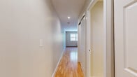 This single-floor residence offers a clean, functional layout with consistent design details throughout. The entryway features a bright hallway with gleaming hardwood floors, recessed lighting, and a sliding barn-style door that adds a modern touch to the space.

The open living and dining area is spacious and airy, centered around warm hardwood flooring that runs throughout the main living spaces. A ceiling fan overhead provides comfortable air circulation, while a large window frames views of surrounding greenery, allowing natural light to fill the room. A wall-mounted air conditioning unit and baseboard heating ensure year-round comfort.

The kitchen is efficiently designed with warm-toned wood cabinetry, granite-style countertops, and tile flooring. It is equipped with a gas range, range hood, and a full-size refrigerator, providing everything needed for everyday cooking. The kitchen flows seamlessly into the living area, creating an open, connected feel.

The bathroom is finished in neutral, light-toned tiles and features a white vanity with ample storage, a mirrored medicine cabinet with a lighted bar, and a glass-enclosed tub and shower combination — offering a clean and classic aesthetic.

Overall, the space presents a cohesive, move-in-ready environment with neutral tones, practical finishes, and an easy-flowing layout suited for comfortable everyday living.
