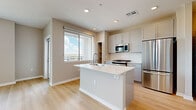 Located on East Camelback Road in Phoenix, Arizona, this one-bedroom, one-bathroom unit offers a thoughtfully designed layout with contemporary finishes throughout. Light wood-style flooring flows through the main living areas, complementing the neutral warm-gray color palette that unifies the space.

The kitchen serves as a functional centerpiece, anchored by a white quartz island with an integrated sink and seating potential. Gray shaker-style cabinetry lines the walls alongside stainless steel appliances, including a gas range, microwave, and refrigerator. A stacked washer and dryer unit is conveniently integrated within the kitchen area. A large window admits natural light and frames outdoor views of the surrounding Phoenix cityscape.

The living area extends from the kitchen, offering an open feel with recessed lighting and access to a private balcony via a glass-panel door, providing additional views of the neighborhood.

The bedroom features plush carpet, a ceiling fan, and a sizable window with city views. It connects to a walk-in closet with built-in shelving and hanging rods, offering organized storage. The bathroom includes a light-toned vanity with a white quartz countertop, an LED-backlit mirror, and wood-style flooring, completing the modern aesthetic of this well-appointed unit.