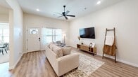 This thoughtfully designed single-story home offers a spacious and cohesive layout with modern finishes and a warm, neutral color palette throughout. The open-concept living, dining, and kitchen area serves as the heart of the home, featuring light wood-look flooring, recessed lighting, and a ceiling fan. The kitchen is outfitted with white shaker cabinetry, quartz countertops, stainless steel appliances, a matte black faucet and pendant lighting over a large center island with bar seating. The dining area is highlighted by a bold abstract canvas, adding a contemporary artistic touch. The primary bedroom features a distinctive tray ceiling with a ceiling fan, plush carpet, and natural light from a window. Its en suite bathroom includes a dual-sink vanity with matte black fixtures, a walk-in tiled shower with marble-style surrounds, and direct access to a spacious walk-in closet with built-in shelving. A dedicated office provides carpeted floors, a ceiling fan, and a bright window. The laundry room includes a utility sink, white cabinetry, and wood-look flooring. Additional highlights include two hallways, a second bathroom, a secondary living room, and an attached two-car garage with an automatic opener.