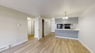 This single-floor unit at 121-221 East Wedgewood in Spokane, Washington offers a well-designed, open-concept layout with consistent wood-style flooring throughout. The living area is generously proportioned, featuring a sliding glass door fitted with vertical blinds that allows natural light to fill the space while providing access to an outdoor area. A baseboard heating system runs along the walls, ensuring year-round comfort.

The kitchen is thoughtfully arranged in a galley-style configuration and opens to the living space via a peninsula with a white countertop and gray accent wall. Gray cabinetry with brushed hardware is featured both above and below the counters, complemented by crisp white countertops, a stainless steel sink, and black appliances including a refrigerator, range, microwave, and dishwasher. A pendant chandelier above the peninsula adds a finishing touch to the kitchen area.

The bedroom features a window with blinds that brings in natural light, wood-style flooring, and baseboard heating. A closet provides convenient storage. The bathroom includes a full tub-shower combination with a white surround, brushed nickel fixtures and grab bars, a vanity with gray cabinetry, and wood-style flooring. Additional rooms offer flexible, open spaces with neutral walls and matching flooring throughout.