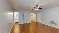 Located at 841 W La Habra Blvd in La Habra, California, this single-floor unit offers a practical and efficiently designed layout comprising a living room, kitchen, and bathroom. The living room serves as the heart of the space, finished with warm wood-style laminate flooring, light gray walls, and a ceiling fan with integrated lighting. A sliding glass door allows natural light to fill the room and provides outdoor access. A wall-mounted HVAC unit ensures climate control, and a built-in closet with sliding doors adds convenient storage. The kitchen is thoughtfully appointed with white cabinetry, granite-look countertops, a stainless-style sink, and a gas range with overhead ventilation — all set atop matching wood-style flooring. The bathroom continues the cohesive aesthetic with a granite-topped vanity, white cabinetry, wood-style flooring, and a full tub-shower combination with clean white tile surround. Throughout the unit, the consistent use of neutral tones, wood-style flooring, and ceiling fans creates a cohesive and functional atmosphere suited for everyday living.
